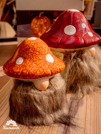 Deux figurines champignons avec chapeaux rouges et oranges, ressemblant à des gnomes, sur une table en bois.